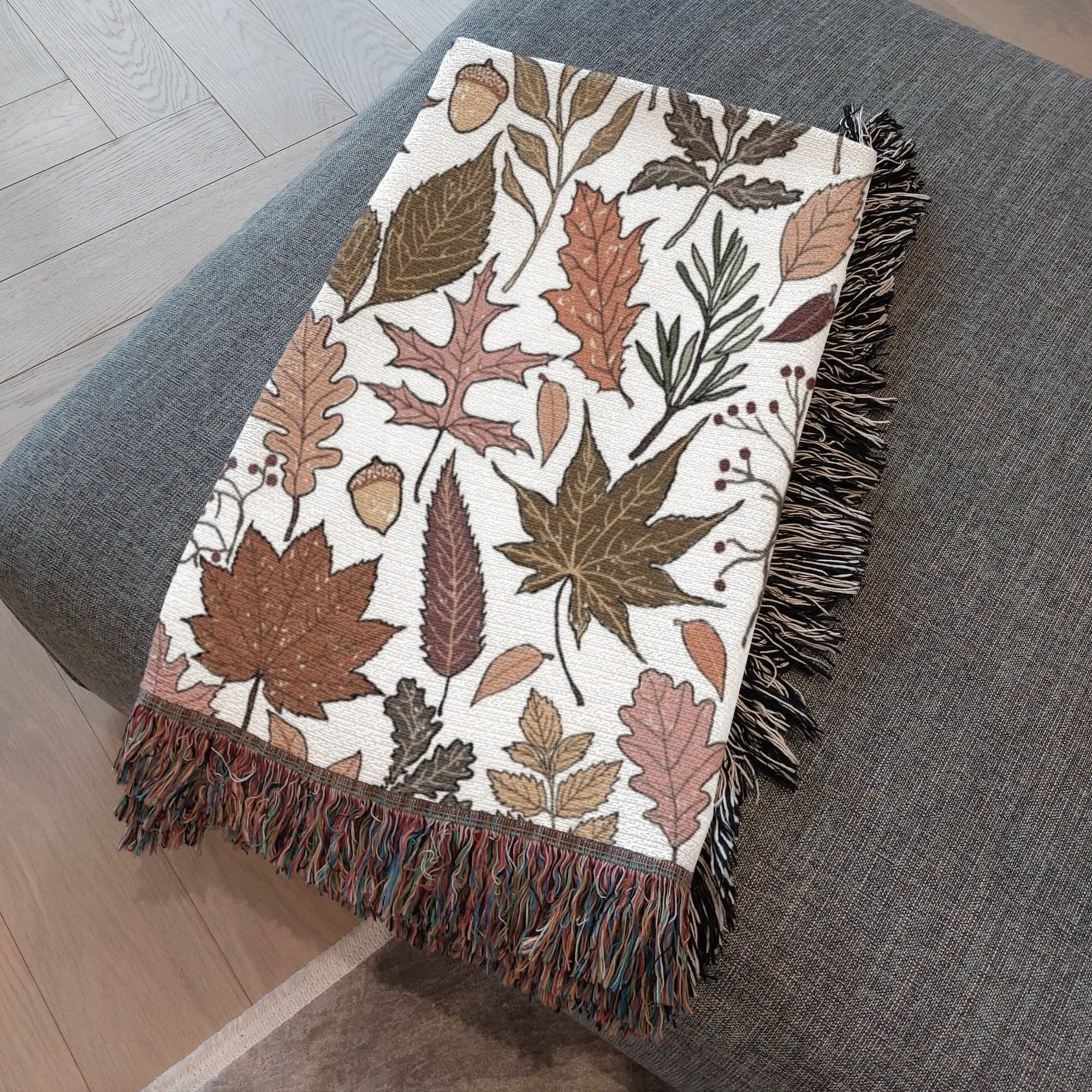 Close-up of orange and yellow, pumpkin spice color  leaves on fall woven blanket cream fabric