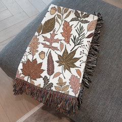 Close-up of orange and yellow, pumpkin spice color  leaves on fall woven blanket cream fabric