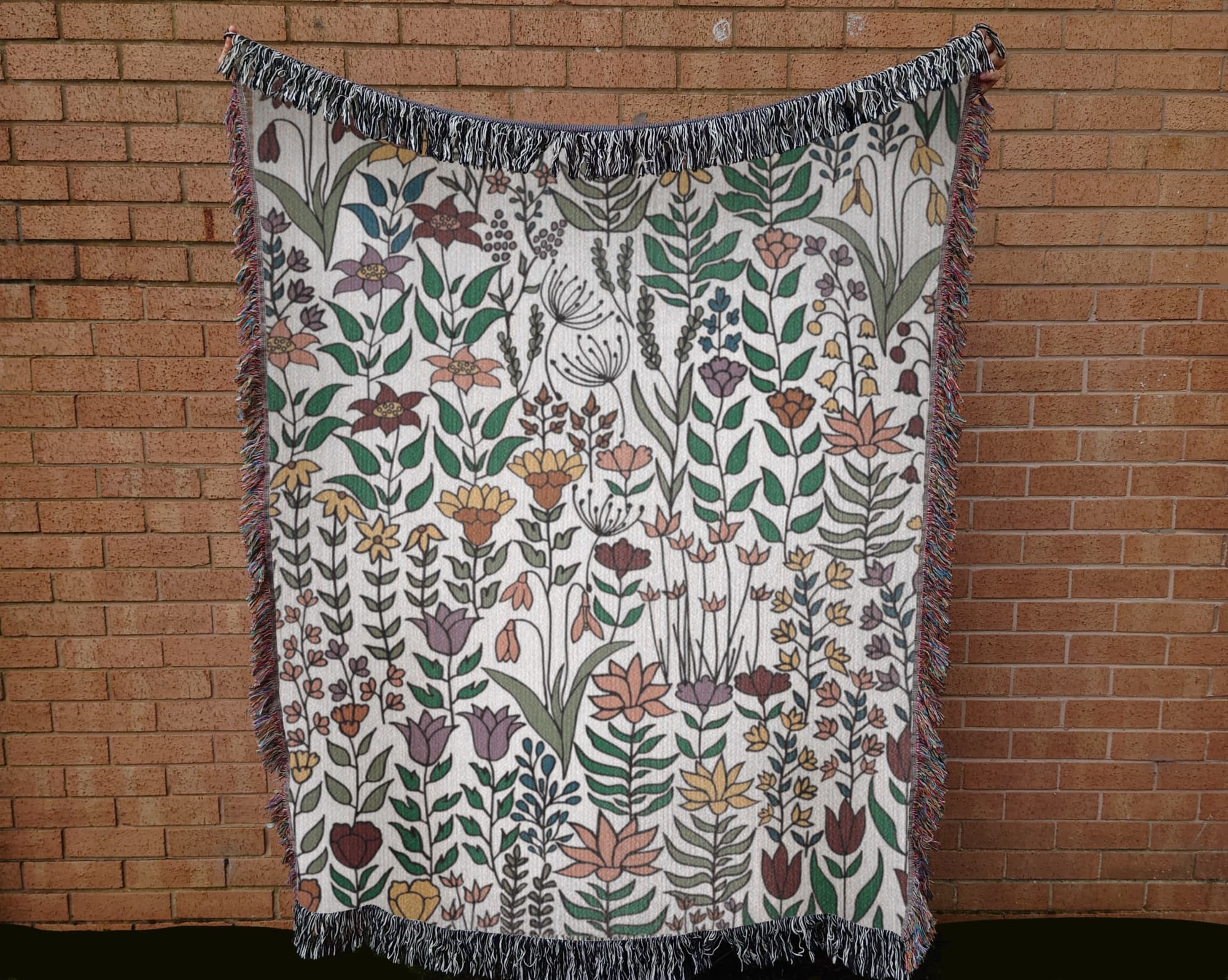 Floral patterned blanket with fringe against a brick wall