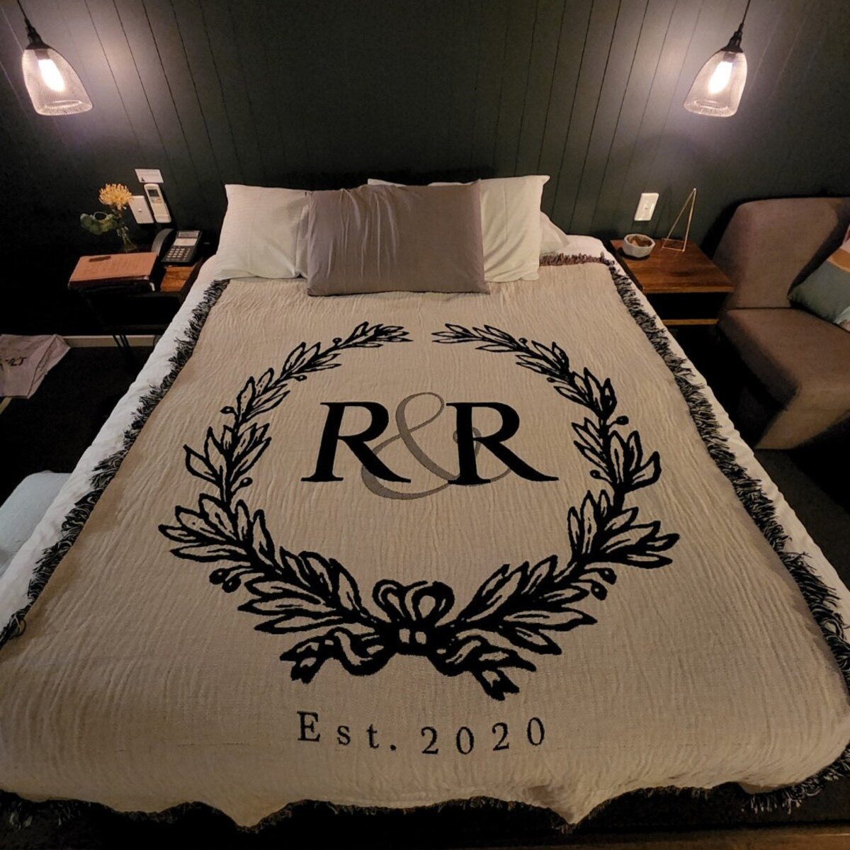 Beige blanket with couple’s initials monogram on a bed in a bedroom setting