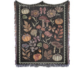 Dark charcoal woven throw blanket featuring pumpkins, mushrooms, fall leaves, and pink bows with fringed edges.