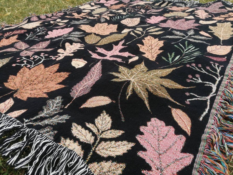 Close-up of rose gold and orange leaves on black autumn tapestry blanket