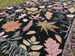 Close-up of rose gold and orange leaves on black autumn tapestry blanket
