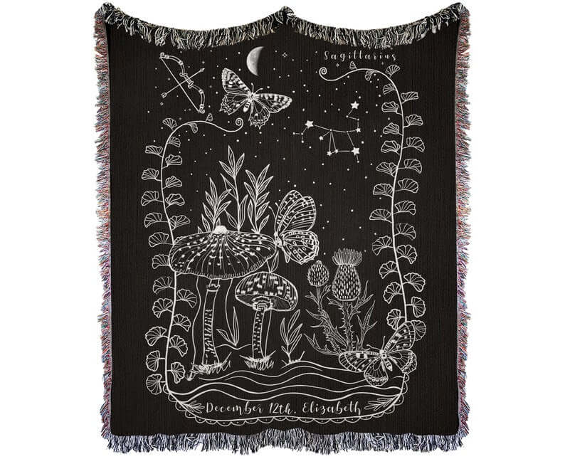 Sagittarius woven blanket featuring intricate designs of mushrooms, butterflies, and stars with colorful fringed edges.