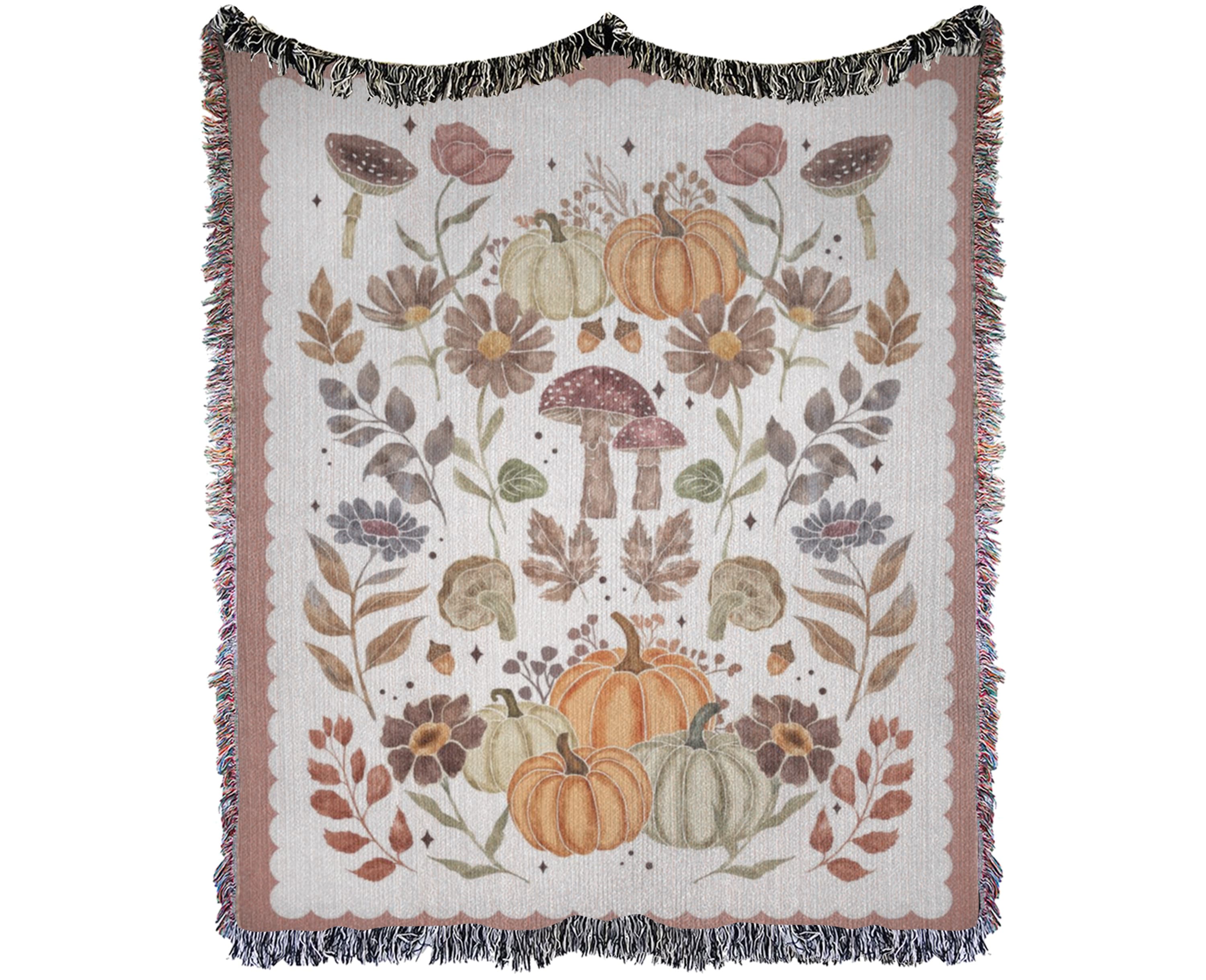 A cotton woven throw blanket with fringe edges, featuring an autumn-themed pattern of pumpkins, mushrooms, leaves, and flowers in muted orange, brown, beige, and gray tones on a cream background.