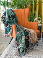 Botanical woven blanket tapestry styled with plants and boho decor accessories
